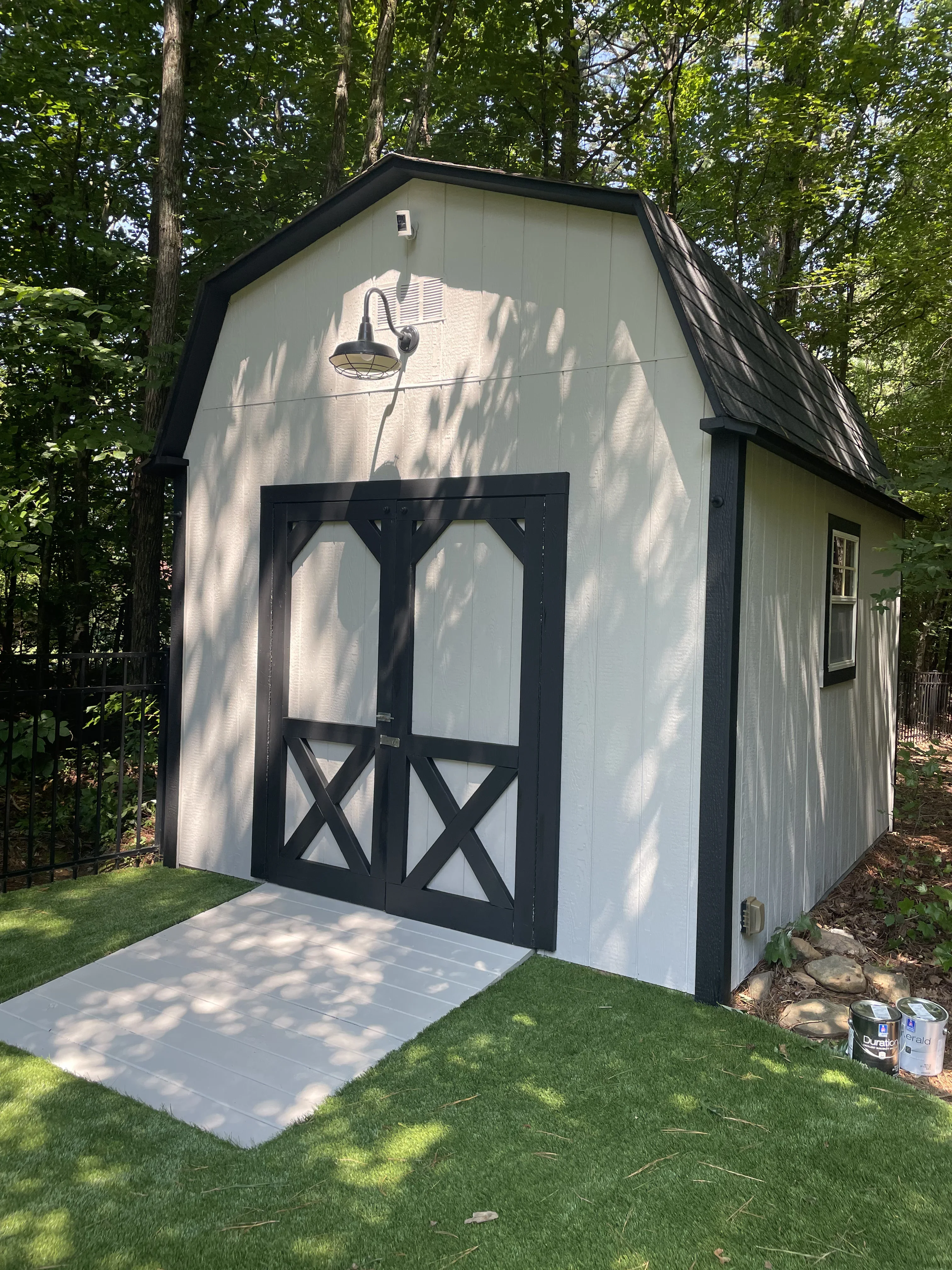 White painted shed with black trim, barn doors, and peaked roof in wooded setting