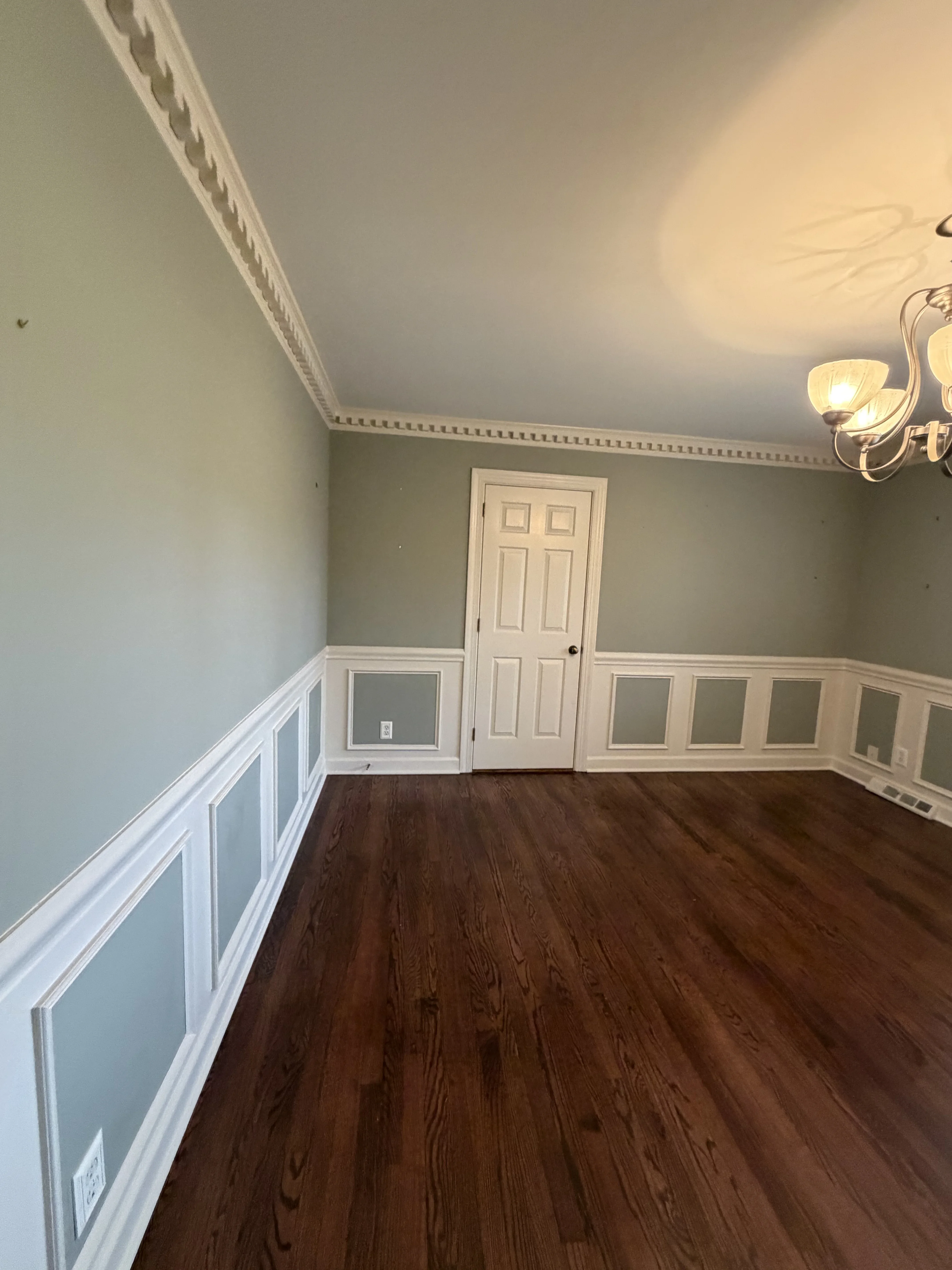 Two-tone painted walls with white wainscoting, crown molding, and dark hardwood floors